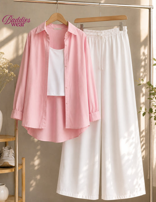 A pink button-up shirt layered over a white tank top, hanging next to a pair of white wide-leg pants on a clothing rack. The image has a warm, sunlit aesthetic with soft shadows, and the 'Baddies wear' brand logo is visible in the top left corner.