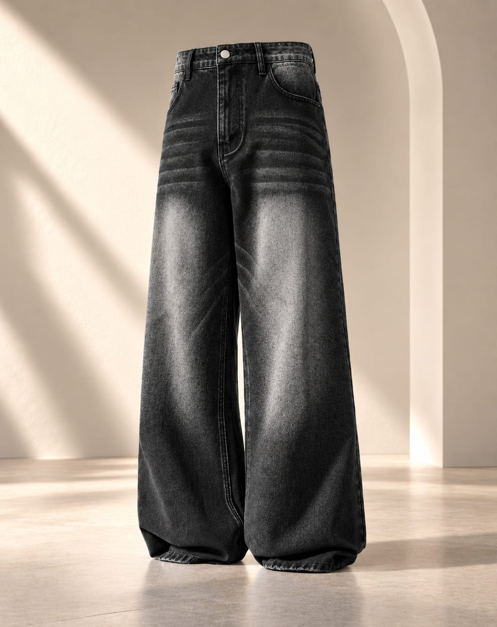 Wide-leg black denim jeans with a faded gray wash and horizontal seam detailing, displayed on a neutral beige studio set with soft architectural shadows.