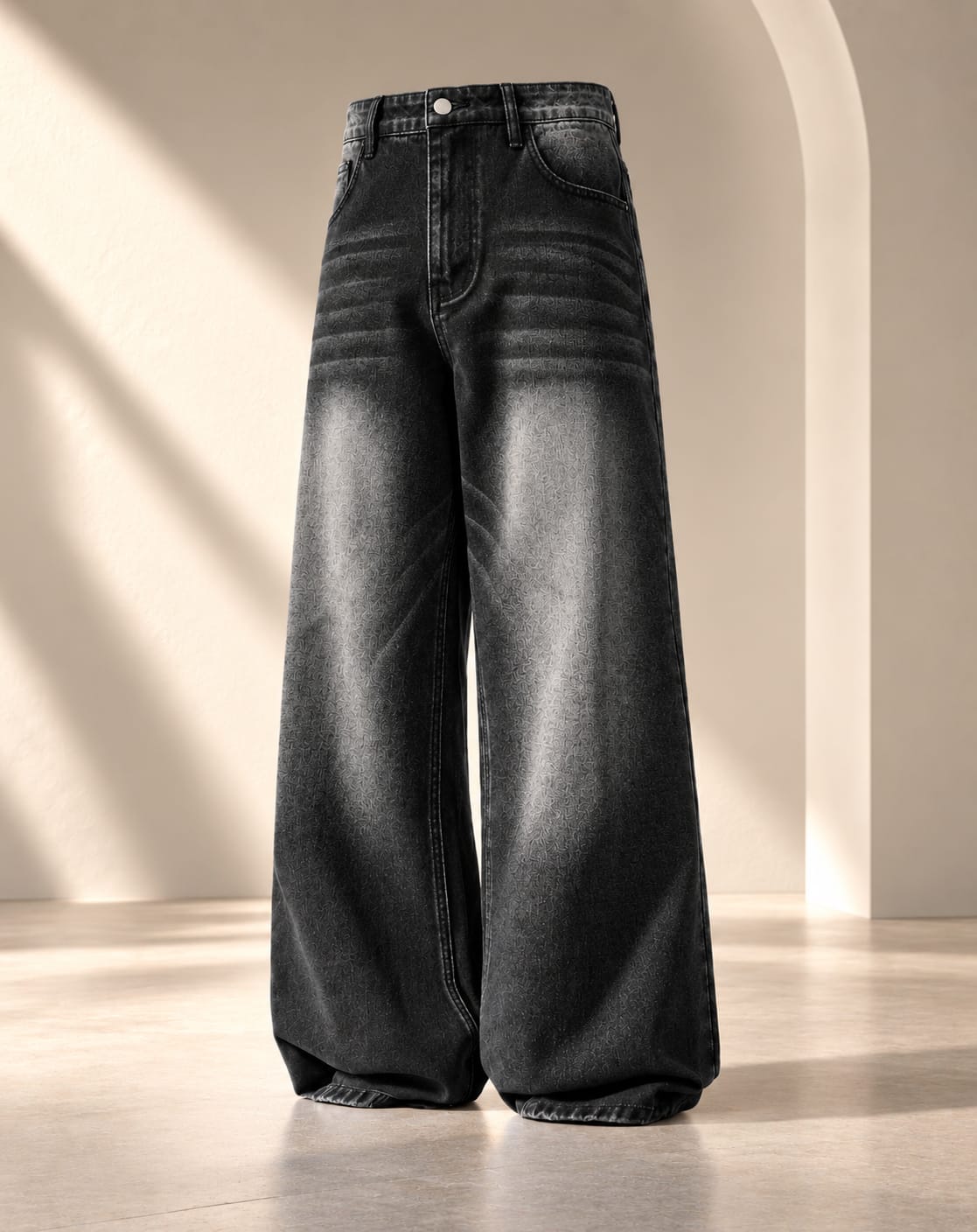 Wide-leg black denim jeans with a faded gray wash and horizontal seam detailing, displayed on a neutral beige studio set with soft architectural shadows.